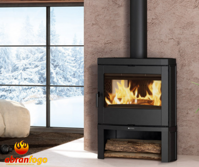 Lareira a lenha em metal preto com madeira e janela nevada ao fundo