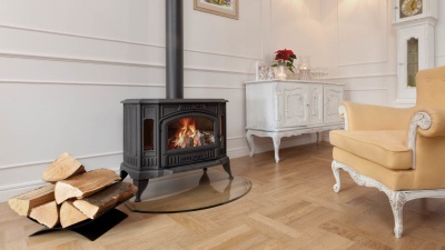 Lareira a lenha com vidro frontal, suporte para lenha e mobiliário clássico numa sala clara.