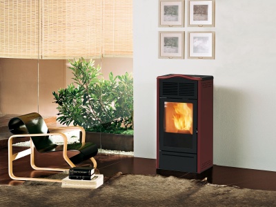 Estufa a pellets preta com vidro mostrando fogo e cadeira de madeira com assento preto num interior com plantas e tapete