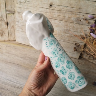 Frasco de cerâmica branco com flores verde-azuladas e fundo de madeira