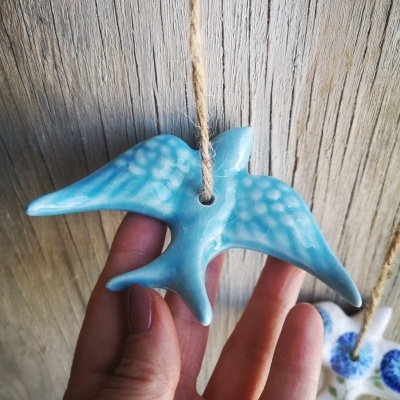 Anzol decorativo azul em cerâmica suspenso por corda com fundo de madeira clara