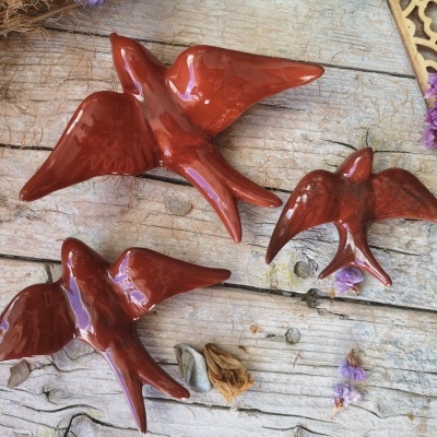 Três pássaros de cerâmica castanha sobre madeira envelhecida com flores secas e painel decorativo