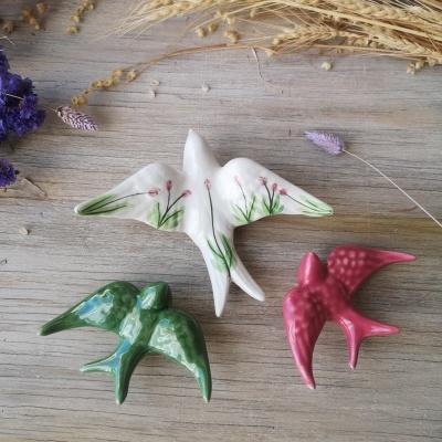 Figuras decorativas de pássaros em cerâmica de várias cores sobre superfície de madeira com flores secas