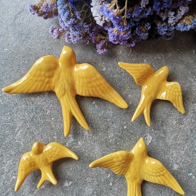 Esculturas de pássaros amarelos de cerâmica sobre fundo cinza com flores roxas secas