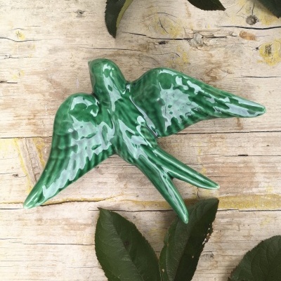 Pássaro decorativo em cerâmica verde brilhante sobre madeira clara com folhas verdes