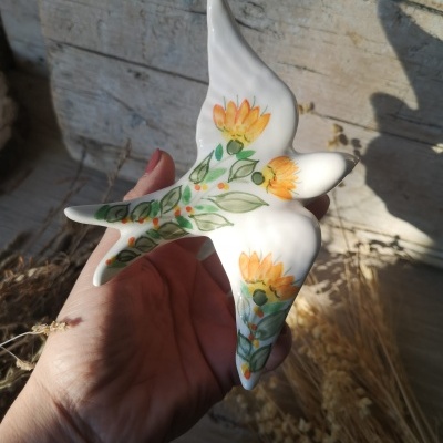Figura de pássaro em cerâmica pintada à mão com flores e folhas, segurada por mão