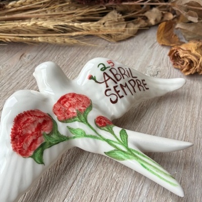 Pomba decorativa em cerâmica branca com flores vermelhas pintadas e texto 25 ABRIL SEMPRE