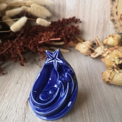 Escultura decorativa em cerâmica azul brilhante sobre madeira clara com flores secas ao fundo