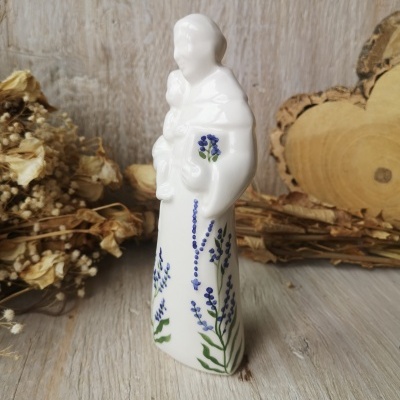 Estatueta de cerâmica branca com flores azuis e verdes sobre superfície de madeira clara.