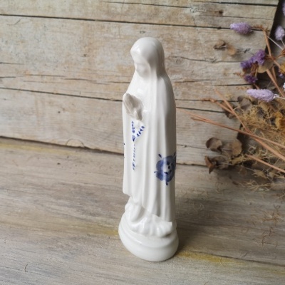 Estátua branca de cerâmica com rosário azul sobre superfície de madeira clara