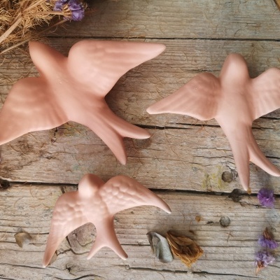 Três pássaros cor-de-rosa em cerâmica sobre madeira rústica com flores secas