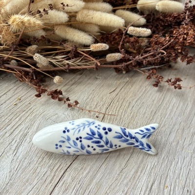 Peixe decorativo em cerâmica branca com padrão azul de folhas e bagas junto a ramos secos