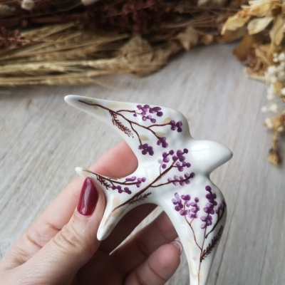 Peça decorativa em cerâmica branca com pintura roxa de flores, forma de pássaro