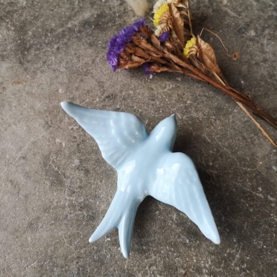 Pássaro decorativo branco em cerâmica junto a flores secas sobre fundo cinzento