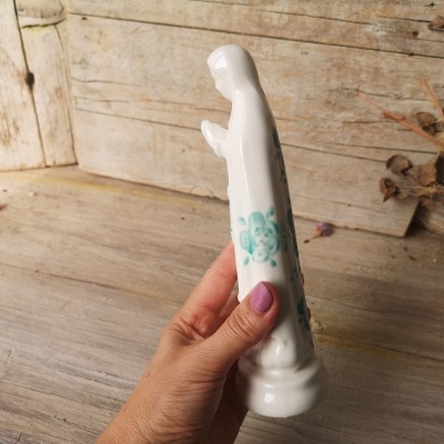 Estátua de porcelana branca com detalhes azuis sendo segurada por mão com unhas lilás