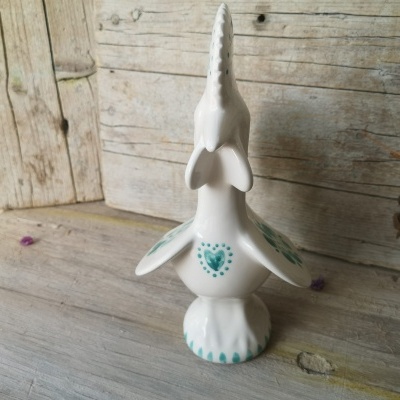 Escultura de cerâmica branca de pássaro com detalhes verdes em madeira