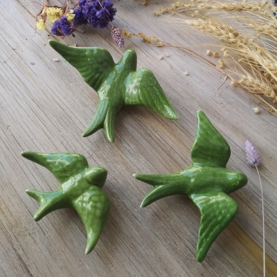Figuras decorativas de pássaros verdes em cerâmica sobre mesa de madeira com flores secas ao redor