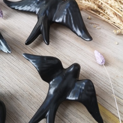 Dois pássaros decorativos pretos sobre madeira com plantas secas ao fundo