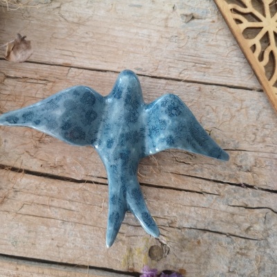 Figura de pássaro azul em cerâmica sobre madeira com flores secas