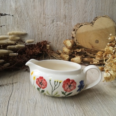 Chaleira de porcelana branca com flores pintadas coloridas e flores secas ao fundo.