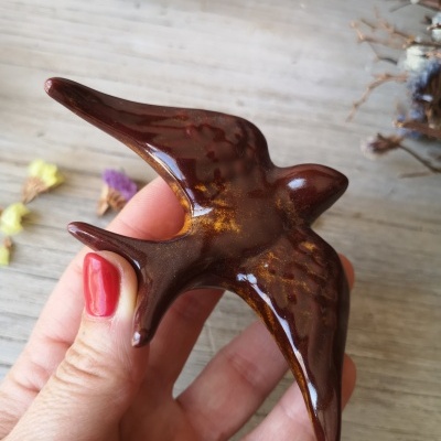 Pássaro decorativo castanho brilhante sendo segurado por uma mão com unhas pintadas de vermelho