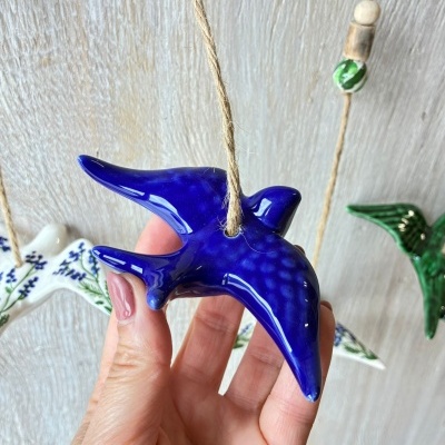 Pássaro decorativo em cerâmica azul pendurado com cordão de juta e contas em fundo claro