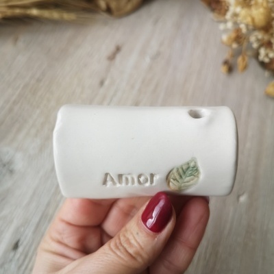 Objeto decorativo branco em cerâmica com a palavra Amor e uma folha verde