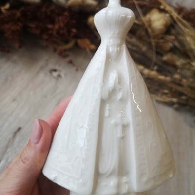 Estatueta branca de Nossa Senhora em cerâmica com manto e coroa, com fundo de madeira e flores secas