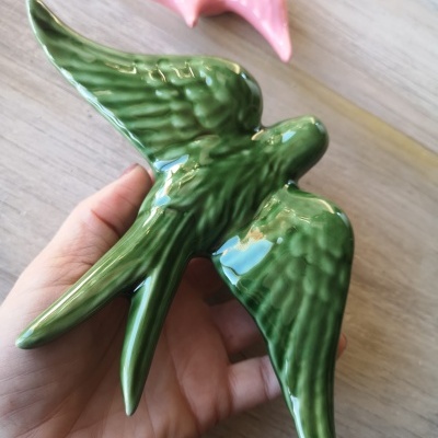 Pássaro decorativo de cerâmica verde brilhante sobre mão com pássaro rosa ao fundo