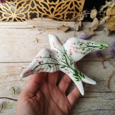 Decoração em cerâmica de pássaro branca com pintura floral em fundo de madeira