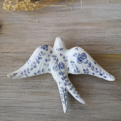 Pássaro decorativo em cerâmica branca com pintura azul floral sobre superfície de madeira