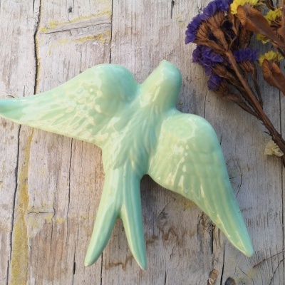 Estatueta cerâmica pássaro azul claro com flores secas num fundo de madeira