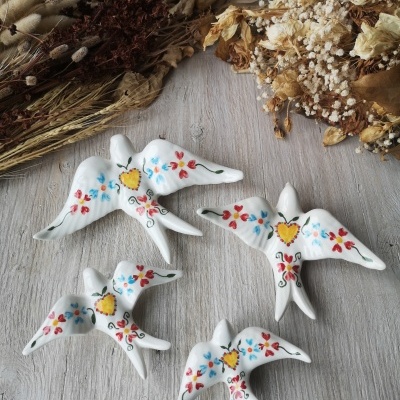 Figuras de pássaros em cerâmica pintadas à mão com flores coloridas em madeira clara e flores secas ao redor