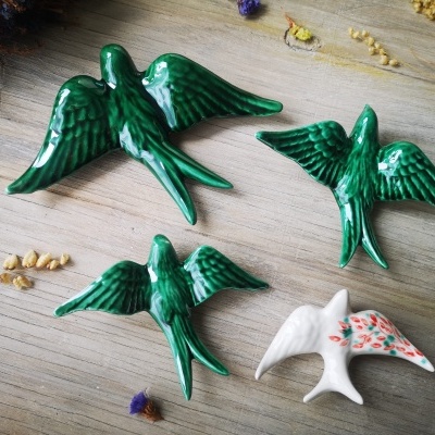 Figuras decorativas de pássaros em cerâmica verde e branca com detalhes florais sobre mesa de madeira