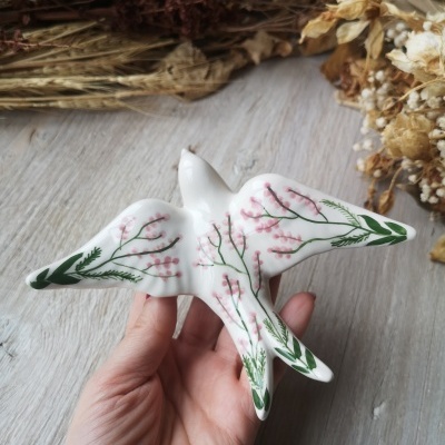 Escultura de cerâmica branca em forma de pássaro com flores rosas e folhas verdes