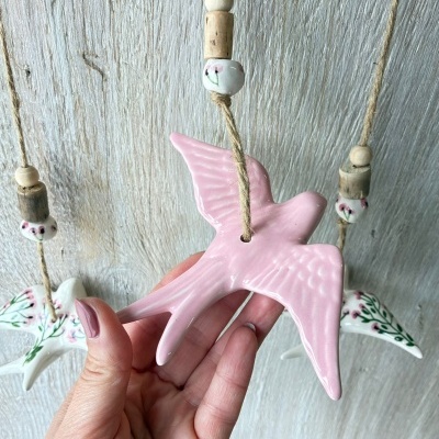Móvel decorativo com pássaros cerâmicos pendurados em corda com contas de madeira e cerâmica pintada.
