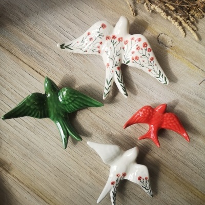 Figuras de cerâmica de pássaros em verde, vermelho e branco com padrões florais, sobre madeira clara.