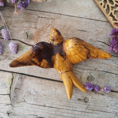 Escultura de madeira de pássaro em voo com acabamento brilhante e flores secas roxas