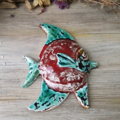 Peixe decorativo de cerâmica vermelho e verde sobre superfície de madeira