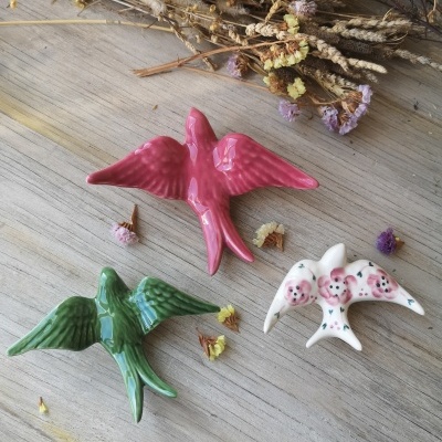 Três pássaros cerâmicos coloridos sobre mesa de madeira com flores secas