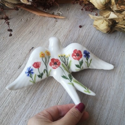 Pássaro decorativo em cerâmica branca com flores pintadas coloridas.