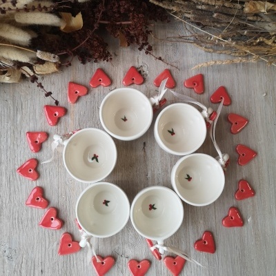 Seis canecas brancas dispostas em círculo com corações vermelhos ao redor e flores secas ao fundo