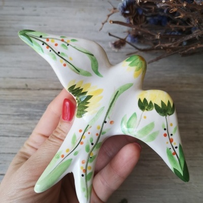 Escultura de cerâmica branca em forma de andorinha com pintura floral colorida