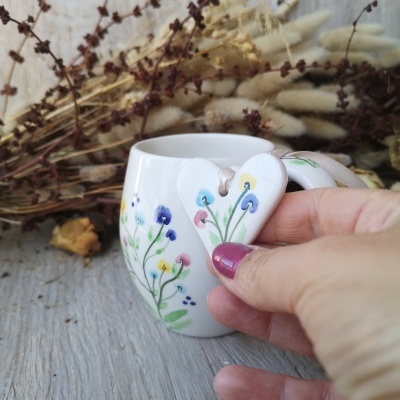 Caneca branca decorada com flores coloridas e etiqueta de coração com flores