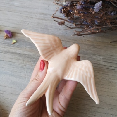 Pássaro decorativo cor de creme em mão feminina com unhas vermelhas junto a raminhos secos de flores