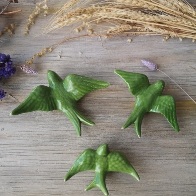 Três pássaros decorativos verdes em cerâmica sobre superfície de madeira com decorações secas