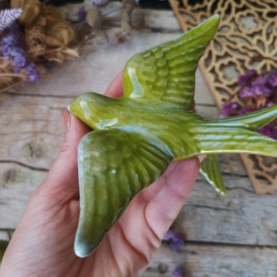 Figura decorativa de pássaro verde em cerâmica nas mãos, com fundo rústico
