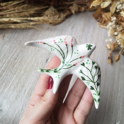 Figurinha de cerâmica de pássaro com pintura floral em fundo com flores secas