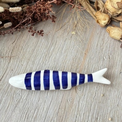 Objeto decorativo em forma de peixe cerâmico azul e branco sobre madeira com ramos secos ao fundo