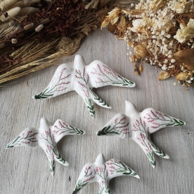 Conjunto de quatro pássaros de cerâmica branca com flores pintadas, em madeira cinzenta com flores secas ao fundo